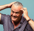 A person with short, grey hair and a jazzy shirt runs Infra Wig, a soft hair styling gel through the top section of their hair.
